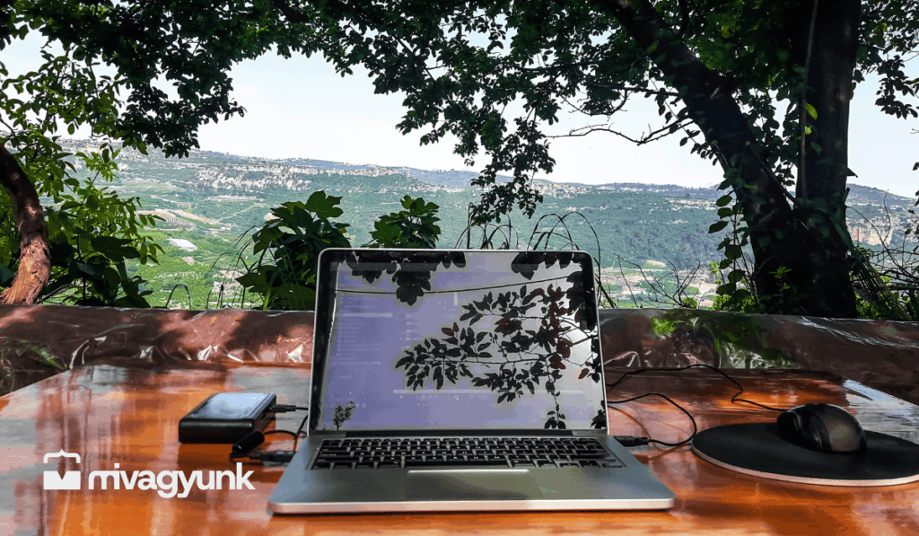 Nyitott laptop egy teraszon, zöld hegyvidéki panorámával a háttérben, szabadúszó munka és MI-használat témájú cikkhez.