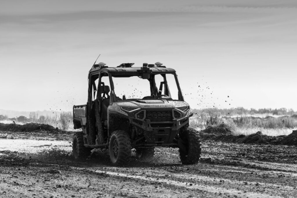Fekete-fehér fotó egy sáros terepen haladó, önvezető képességű Polaris terepjárműről, amely autonóm földi járművek katonai tesztelését és harctéri logisztikai használatát illusztrálja.