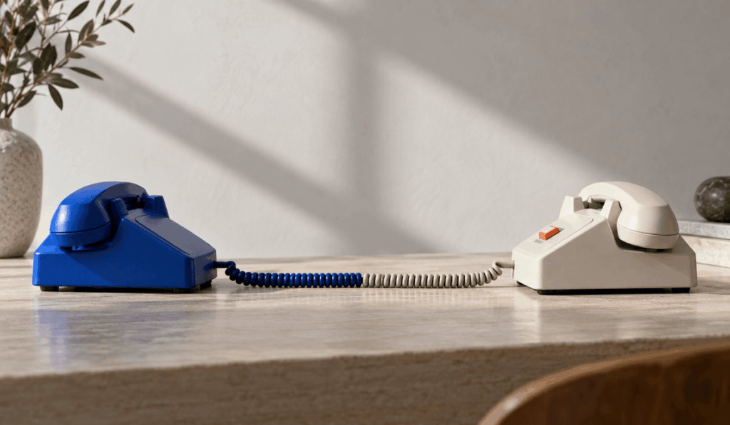 Két retro telefon egy asztalon, az egyik indigókék, a másik törtfehér narancsszínű gombbal, a készülékeket összekötő vezetékkel – az USA és Kína közötti MI-incidenskommunikáció jelképeként.