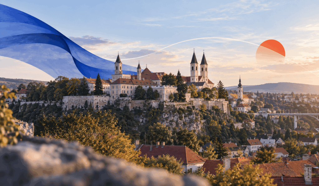 Veszprém vára és történelmi belvárosa naplementében, dombtetőn álló templomtornyokkal, vörös tetőkkel és finom kék-narancs grafikai elemekkel a képen.